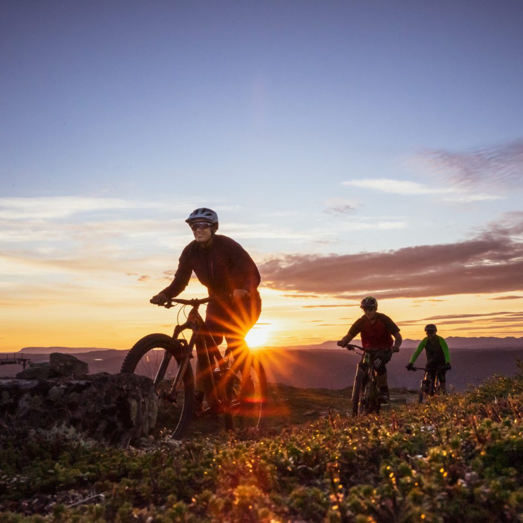 Bilde av tre personer som sykler Hallingspranget i solnedgang