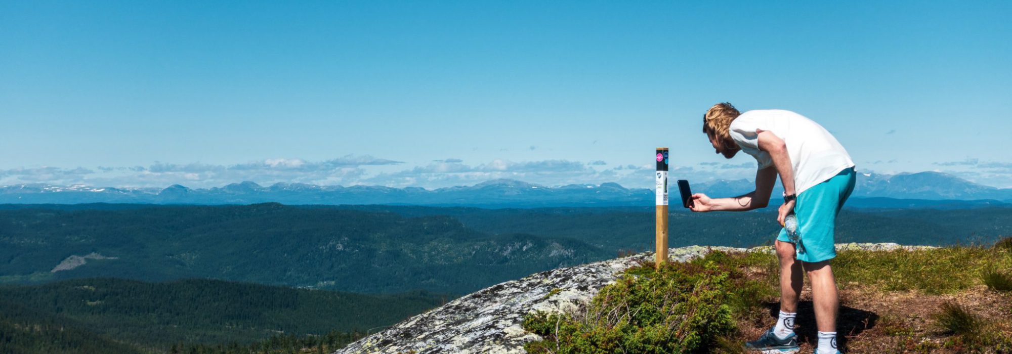 Bilde av en som scanner en stolpe på en fjelltopp